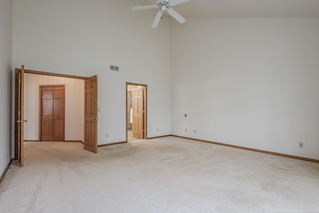 spare room with a high ceiling, a ceiling fan, visible vents, baseboards, and light colored carpet