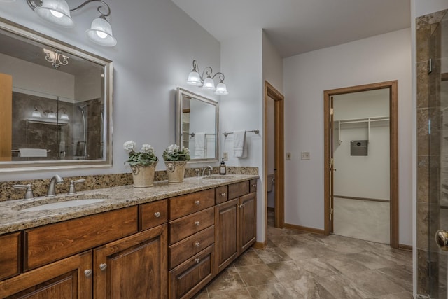 bathroom with a walk in closet, a tile shower, double vanity, and a sink