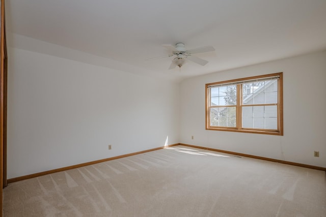 spare room with a ceiling fan, light colored carpet, and baseboards