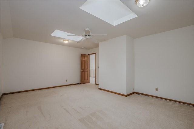 empty room featuring baseboards, a skylight, ceiling fan, and light carpet