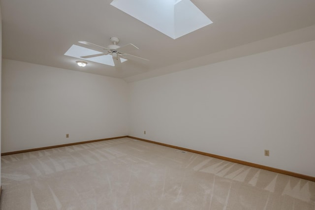 unfurnished room featuring ceiling fan, vaulted ceiling with skylight, light colored carpet, and baseboards