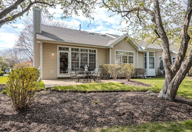 back of property featuring a chimney, roof with shingles, a yard, and a patio area