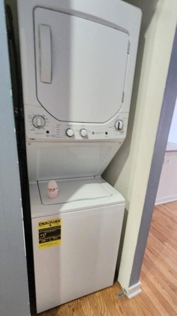 clothes washing area with laundry area, baseboards, stacked washer / dryer, and light wood-style floors