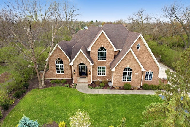 traditional home with brick siding, a shingled roof, and a front lawn