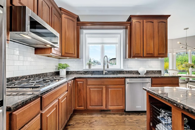 kitchen with dark stone countertops, backsplash, wood finished floors, a sink, and appliances with stainless steel finishes