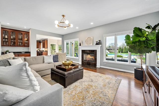 living room with baseboards, recessed lighting, a notable chandelier, a tile fireplace, and dark wood-type flooring