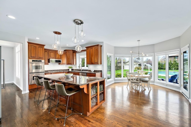 kitchen with a center island, a chandelier, backsplash, appliances with stainless steel finishes, and dark wood-type flooring