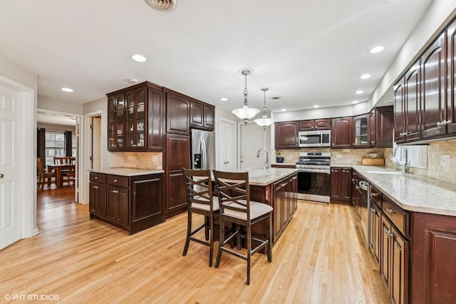 kitchen with stainless steel appliances, dark brown cabinets, a sink, and light wood-type flooring