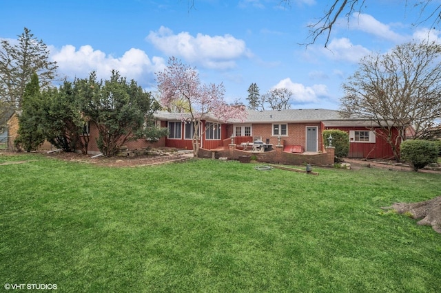 back of house featuring a lawn, a patio, a sunroom, and brick siding