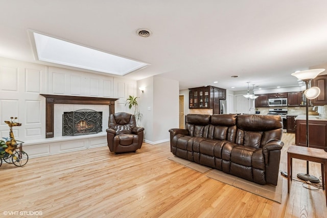 living room featuring light wood-style floors, baseboards, a high end fireplace, a skylight, and visible vents