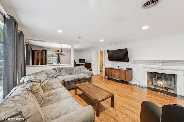 living room with visible vents, crown molding, a high end fireplace, light wood-type flooring, and a notable chandelier