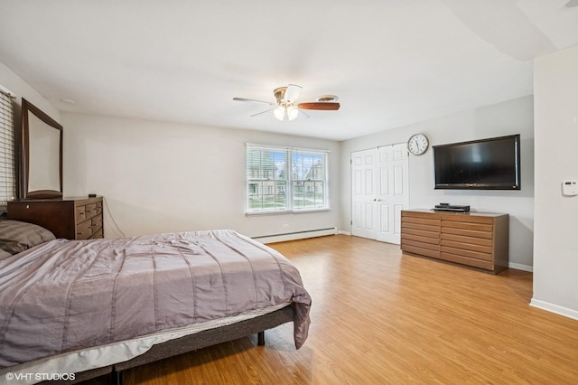 bedroom featuring ceiling fan, light wood-style floors, baseboards, a baseboard heating unit, and a closet