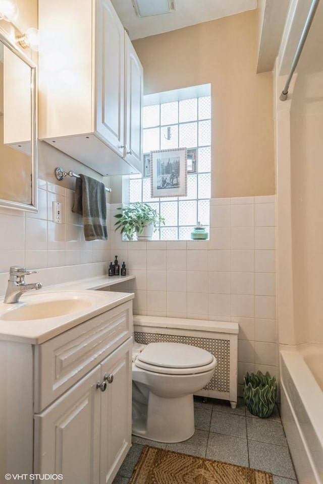 full bath with tile patterned flooring, vanity, toilet, a wainscoted wall, and tile walls