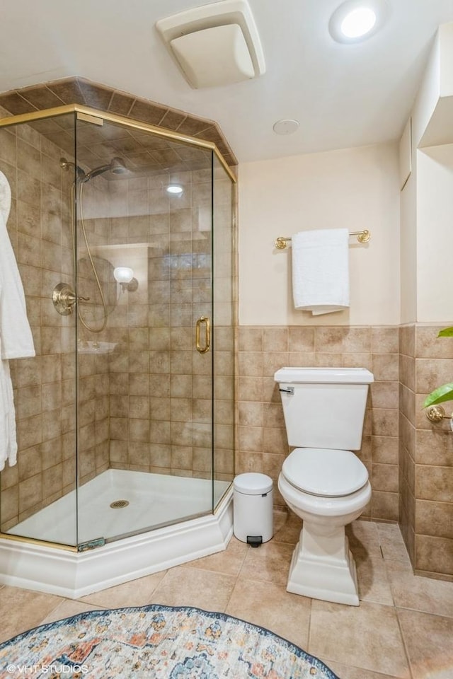 bathroom featuring wainscoting, toilet, tile patterned floors, and a shower stall