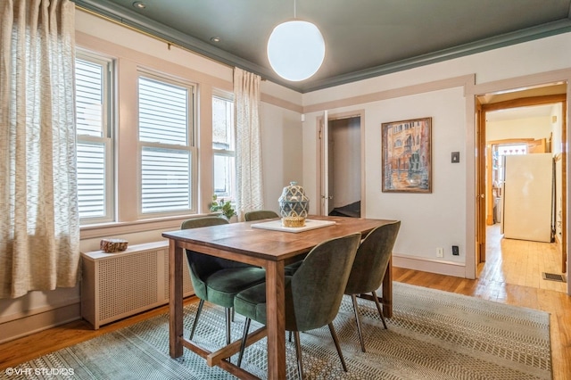 dining room featuring visible vents, baseboards, light wood-style floors, radiator, and ornamental molding