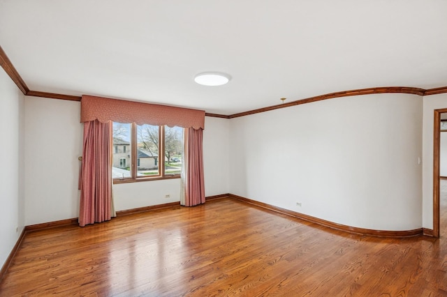 empty room featuring crown molding, baseboards, and wood finished floors