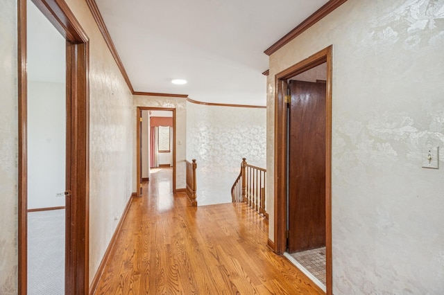 hallway featuring crown molding, light wood-style floors, baseboards, and an upstairs landing