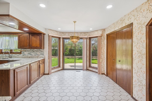 kitchen with a notable chandelier, light stone counters, a sink, wallpapered walls, and light floors