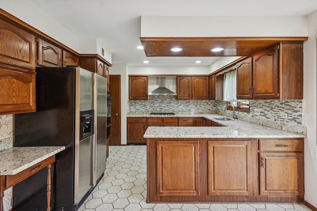 kitchen with a peninsula, stainless steel refrigerator with ice dispenser, wall chimney exhaust hood, gas stovetop, and a sink