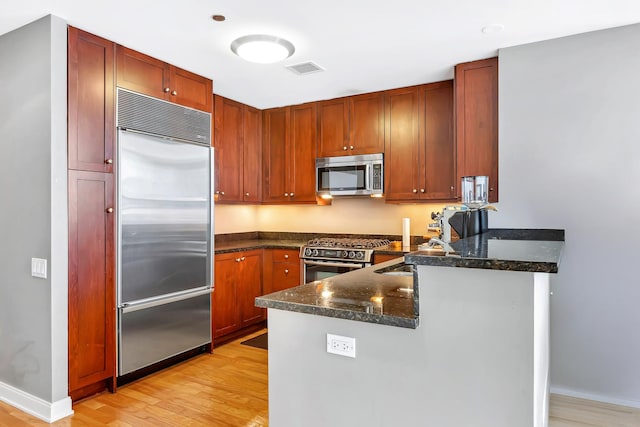 kitchen featuring a peninsula, dark stone countertops, a sink, light wood-style flooring, and appliances with stainless steel finishes