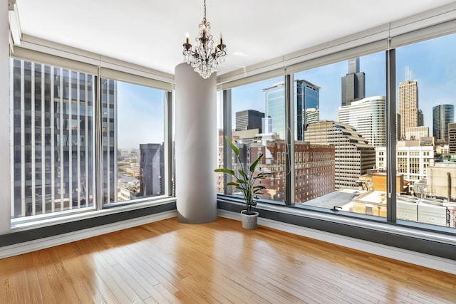 unfurnished room featuring an inviting chandelier, a view of city, and hardwood / wood-style flooring