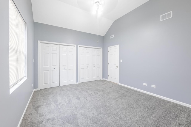 unfurnished bedroom featuring carpet flooring, lofted ceiling, visible vents, baseboards, and multiple closets