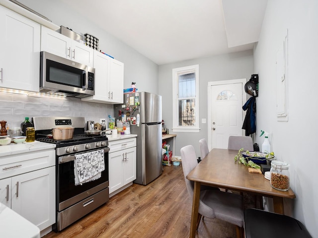 kitchen with white cabinets, light wood finished floors, stainless steel appliances, backsplash, and light countertops