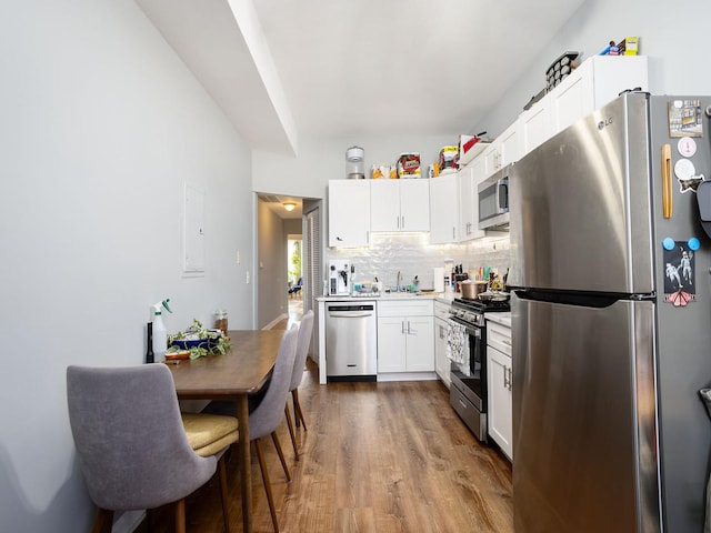 kitchen with dark wood finished floors, light countertops, backsplash, appliances with stainless steel finishes, and white cabinetry