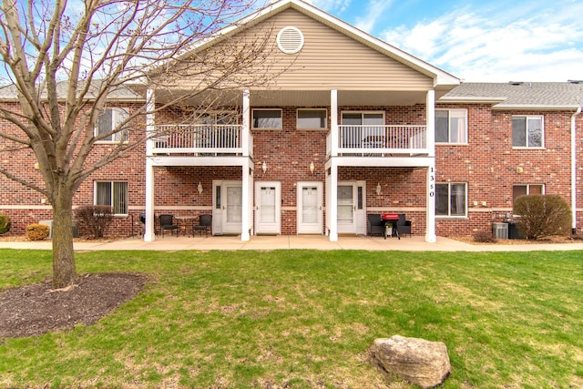 rear view of house featuring a lawn, a balcony, and brick siding