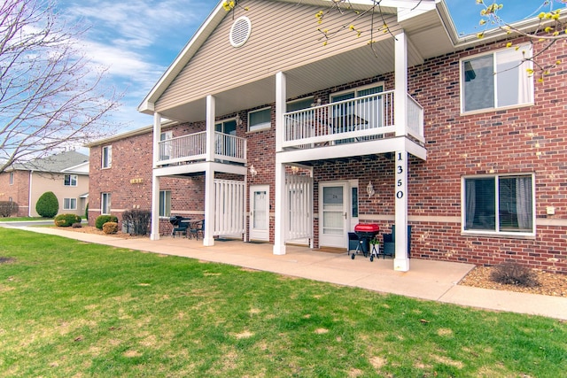 rear view of house featuring brick siding, a yard, and a balcony