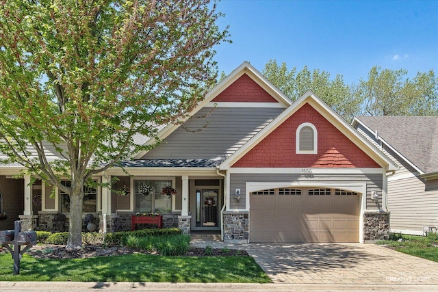 craftsman house featuring covered porch, an attached garage, stone siding, and driveway