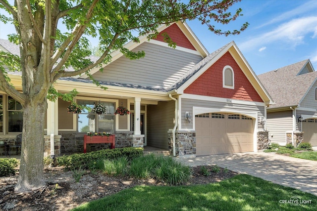 craftsman house featuring stone siding, a garage, a porch, and decorative driveway