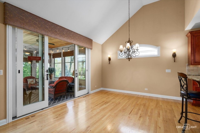 dining space with light wood-type flooring, healthy amount of natural light, a chandelier, baseboards, and high vaulted ceiling