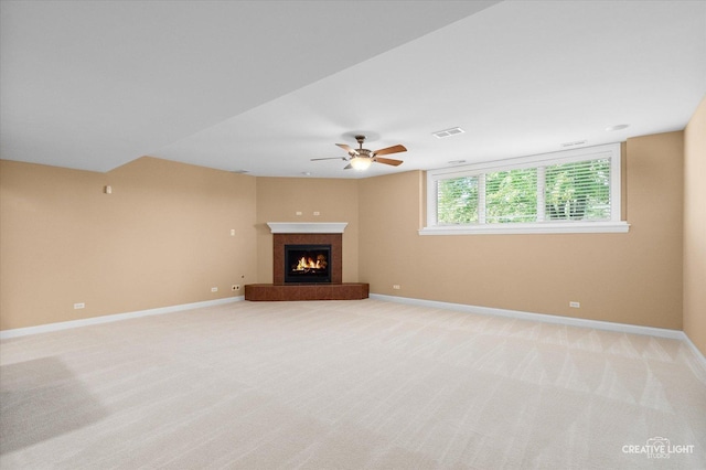 unfurnished living room featuring a lit fireplace, baseboards, ceiling fan, and light colored carpet