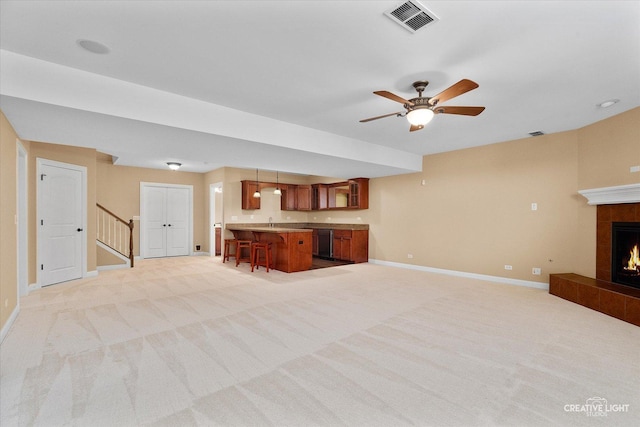 unfurnished living room featuring light colored carpet, baseboards, a fireplace, stairs, and a ceiling fan