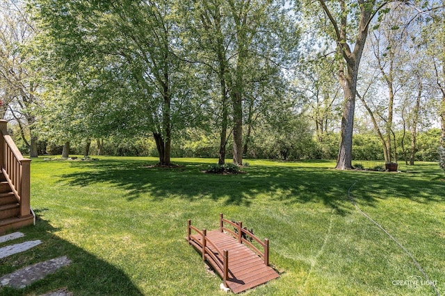view of green lawn featuring view of wooded area and stairs