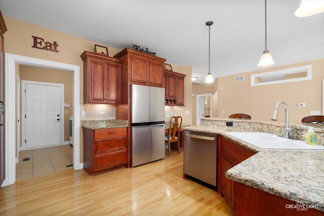 kitchen featuring stainless steel appliances, a sink, pendant lighting, light wood finished floors, and light stone countertops