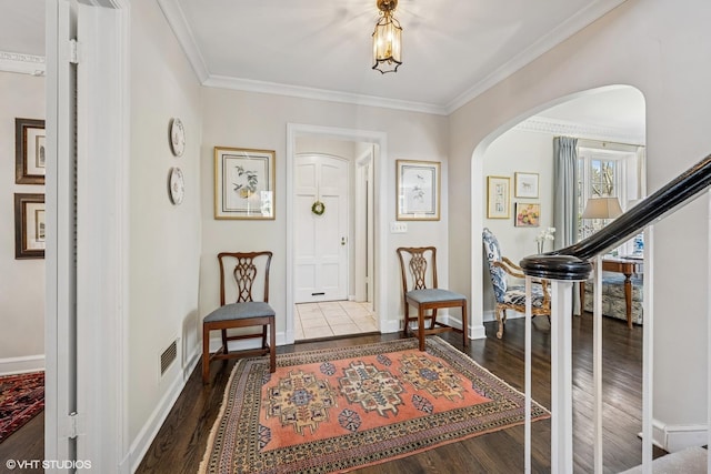 entryway with visible vents, crown molding, wood finished floors, baseboards, and arched walkways