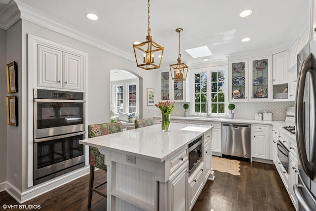 kitchen featuring recessed lighting, tasteful backsplash, arched walkways, appliances with stainless steel finishes, and a skylight