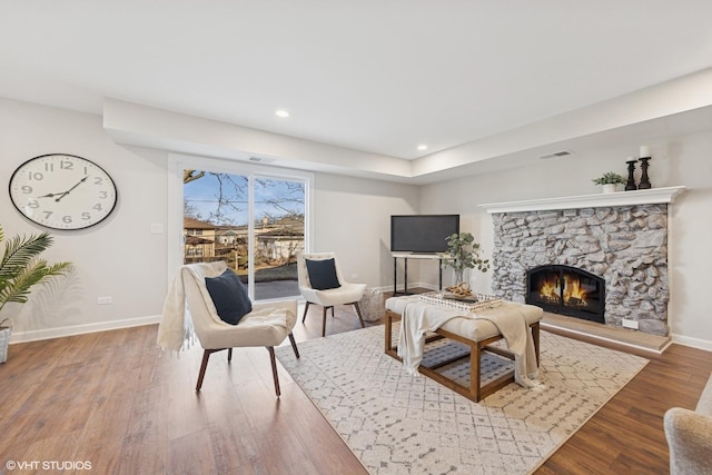 living room with baseboards, visible vents, recessed lighting, wood finished floors, and a stone fireplace