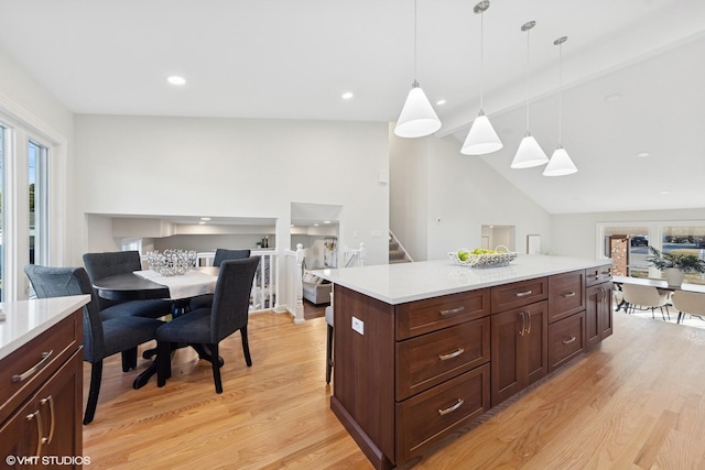 kitchen featuring lofted ceiling, light countertops, light wood-style floors, hanging light fixtures, and open floor plan