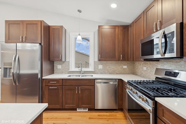kitchen with a sink, light wood-type flooring, backsplash, lofted ceiling, and appliances with stainless steel finishes