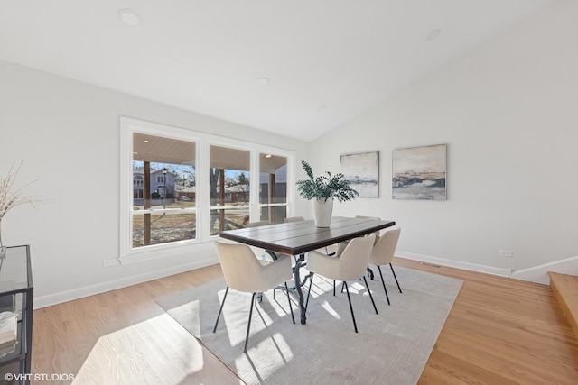 dining room with vaulted ceiling, baseboards, and light wood-type flooring