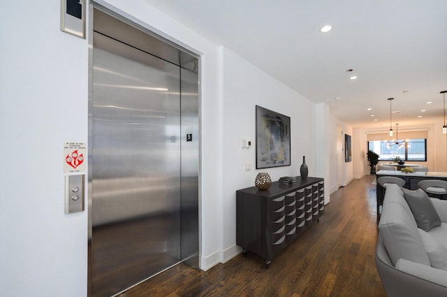 hallway featuring recessed lighting, wood finished floors, elevator, baseboards, and a notable chandelier