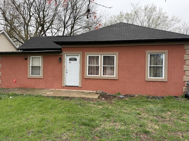 exterior space with roof with shingles, a front yard, and stucco siding