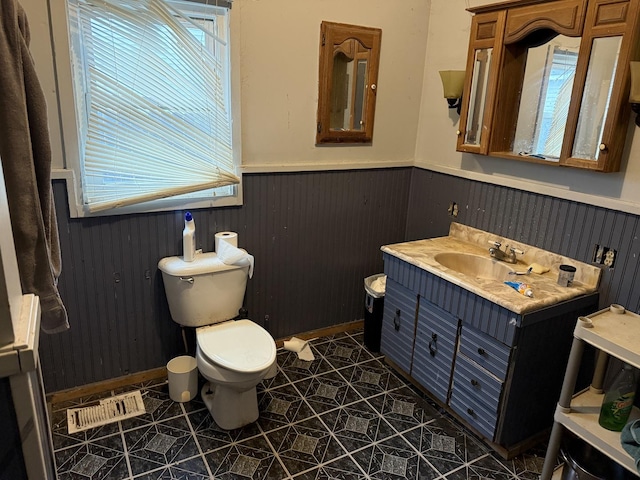 half bathroom featuring a wainscoted wall, toilet, visible vents, tile patterned flooring, and vanity
