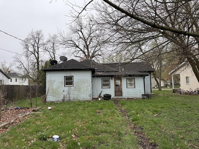 rear view of property featuring a yard, roof with shingles, and fence