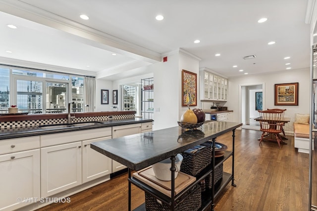 kitchen with crown molding, dark countertops, a sink, dark wood-style floors, and white cabinetry