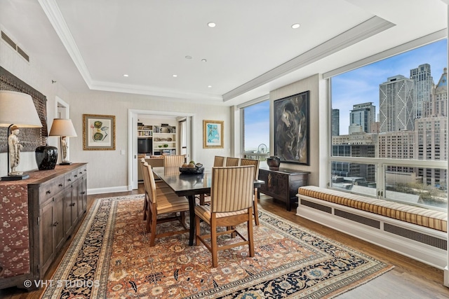 dining space with visible vents, ornamental molding, wood finished floors, baseboards, and a raised ceiling