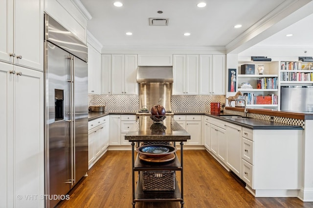 kitchen with a sink, extractor fan, dark countertops, and stainless steel built in refrigerator